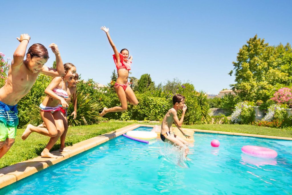 teenagers jumping into a backyard swimming pool