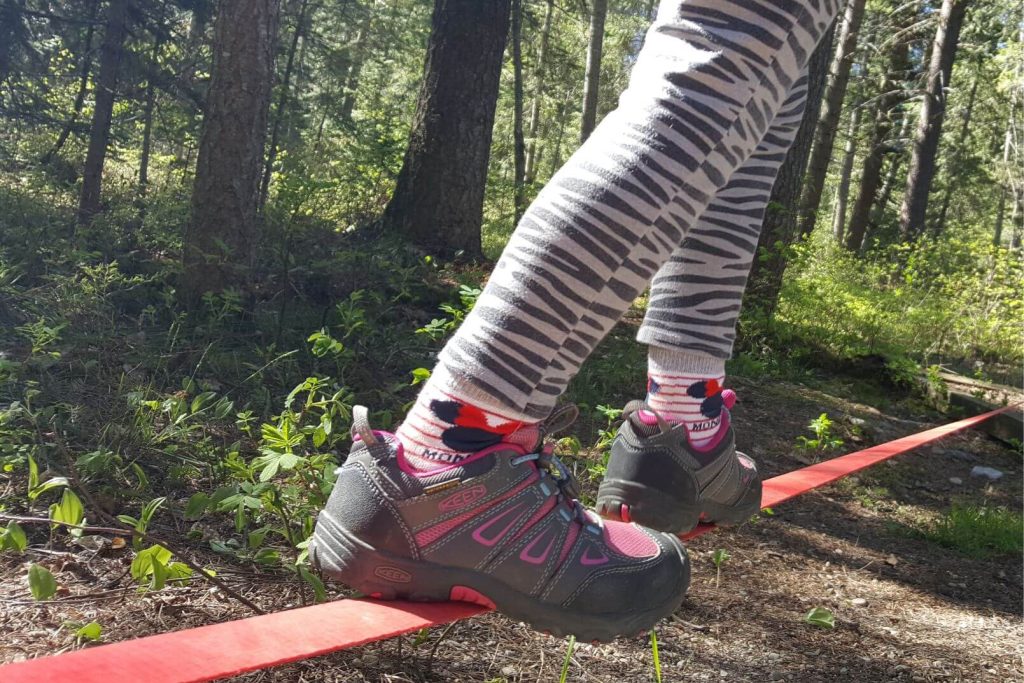close up of a kid's shoes on a slackline, trees in the background